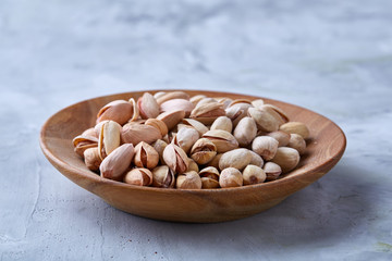 Salted pistachios on a wooden plate over white background, top view, close-up, selective focus.