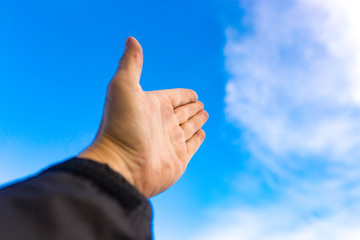 Male hand against a blue sky with clouds