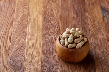 Unpeeled peanuts in wooden bowl over rustic wooden background closeup, selective focus