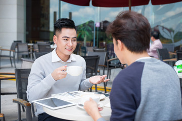 Two young handsome businessmen in casual clothes smiling, talking in coffee shop.