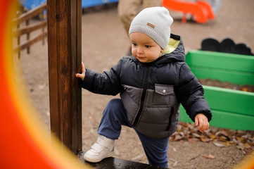 Cute boy dressed in warm clothes walking on the playground