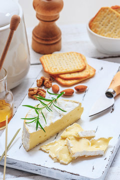 Cheese plate served with crackers, honey and nuts. Camembert on white wood serving board over white texture background. Appetizer theme.