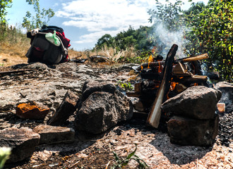 A view of a buning bonfire and a full touristic packpack. The photo was shot one summer day on the...