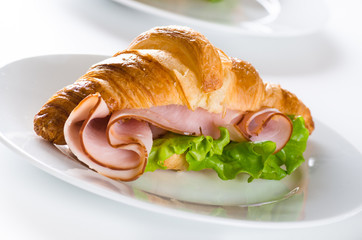 Fresh croissant with ham and salad leaf on white