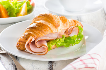 Fresh croissant with ham and salad leaf with sfresh salad on white wooden background