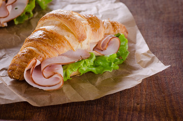 Fresh croissant with ham and salad leaf on dark wooden background