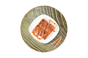 Biscuit cake with caramel syrup on white plate with cinnamon sticks on wooden background, top view, copy space, flat lay,