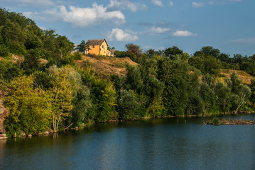 Fototapeta na wymiar A beautiful summer view of a green hill with a small yellow house, located on the riverbank, Gordashovka village, Ukraine.
