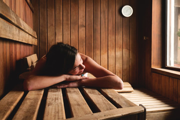 A beautiful woman wearing a white towel takes a sauna: The sauna is made of wood with a large...