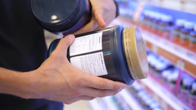 Sportsman Reading Label On BCAA Sport Nutrition Checking Ingredients In Pharmacy