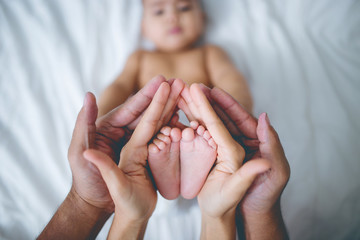 Hands of parents holds baby feet on the bed.