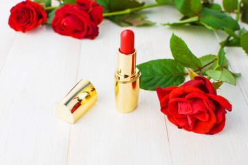 Obraz na płótnie Canvas Red lipstick with red roses on a white wooden background with copy space. Makeup Accessories Selective focus. Various cosmetic products for make-up.