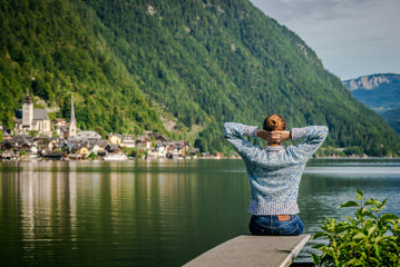 Fototapeta na wymiar girl is sitting on wooden bridge. Young tourist woman sits on the bridge and enjoy the relaxation and freedom. Beautiful view of the mountain nature. wonderful view of Hallstatt. bridge over lake 
