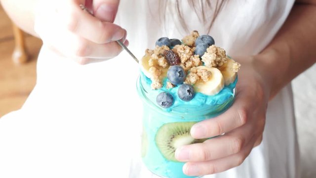 female hands holding overexposed blue majik, eating summer spirulina smoothie