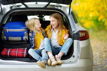 Two adorable girls with a suitcase going on vacations with their parents. Two kids looking forward for a road trip or travel. Autumn break at school.
