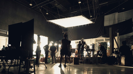 Behind the scenes of silhouette people working in big production studio with professional set and lighting for making movie film or video commercial. - obrazy, fototapety, plakaty