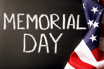 Memorial day weekend text written on wooden black chalkboard with USA flag. United States of America stars & stripes patriot veteran remembrance symbol. Background, close up, copy space, top view.