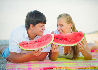 Happy loving couple on a picnic eating a watermelon in white clothes on the beach, a holiday sunny day