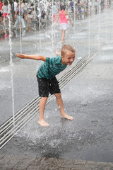 Little happy boy has fun in outdoor fountain at hot day