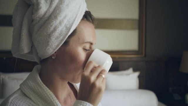 Woman drinks coffee on sunny morning in the room on the bed