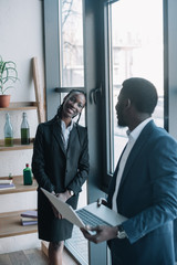 smiling african american businessman with laptop and colleague near by in cafe