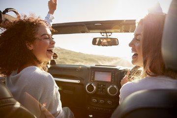 Young adult girlfriends having fun driving an open top car