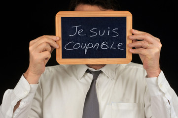 Homme cachant son visage avec une ardoise sur laquelle est écrit je suis coupable 