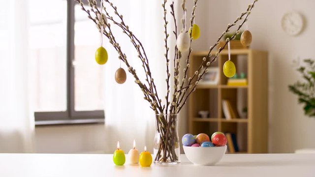 easter, religious holidays and traditions concept - decorated pussy willow in vase, colored eggs and candles burning on branch sunday at home