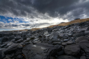 Fototapeta premium Black rocks on the coast of Iceland with small houses abandoned in the background