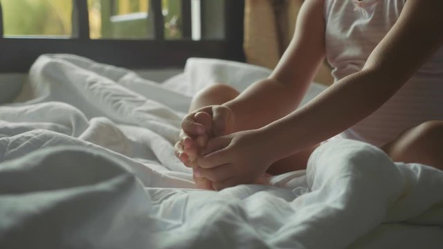 Close-up of baby girl sits on the bed and touching her foot in slow motion