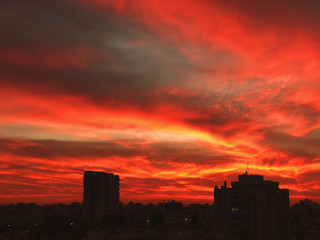 Sunset in the city with stunning colorful magic clouds. Spring sky with red clouds and roofs view.