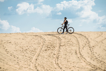 Fototapeta na wymiar Female mountainbiker in desert. Fit sport woman wearing sportswear standing with her bicycle. Extreme games. Desert trip.