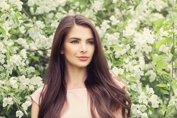 Fashion Portrait of Young Brunette Woman with Long Brown Hair and Makeup on Blossom Spring Flowers Background