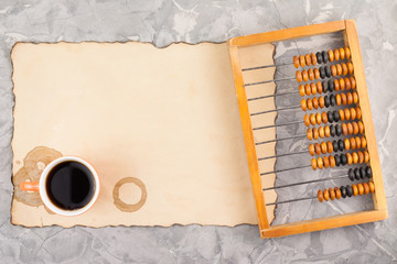 Old wooden scratched abacus and red mug of black tasty coffee on rectangle burnt empty paper with...