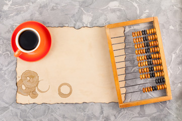 Old wooden scratched abacus and mug of black tasty coffee on red saucer on rectangle burnt empty...