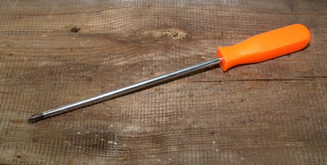 Phillips screwdriver with orange handle on a wooden background close-up