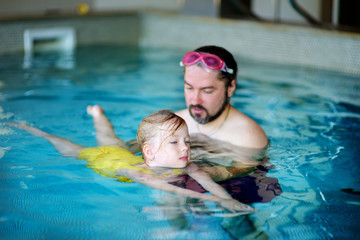Happy father teaching his little daughter to swim. Active happy child learning to swim.