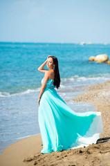 Fototapeta na wymiar Young woman in a blue dress is walking along the beach