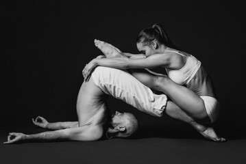 Fototapeta na wymiar Monochrome portrait of beautiful sporty couple: woman and man in white clothes doing yoga asanas together indoor 