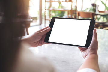 Mockup image of woman's hands holding black tablet pc with blank white desktop screen on table in cafe