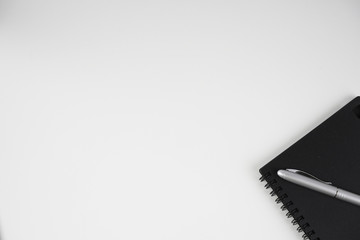 Flat lay image of black book and silver pen over white background