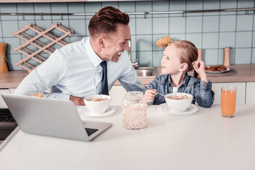 Interesting story. Positive delighted male person turning head while listening to his kid and being at home
