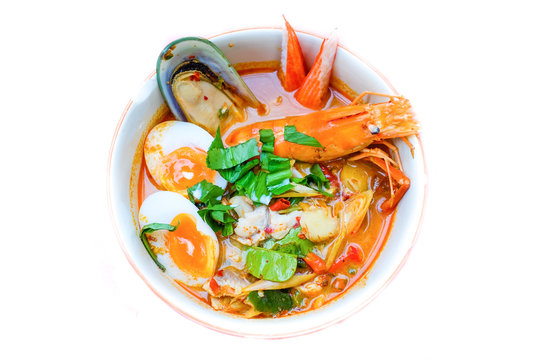 Thai noodle soup (Tom Yum Soup Recipe) with shrimp, dumpling fish, New Zealand mussels, crab and egg (onsen tamago) serve on white bowl for Thai food background or texture.