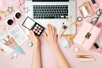 Fashion blogger working with laptop. Workspace with  female accessory, cosmetics products on pale pink table. flat lay, top view