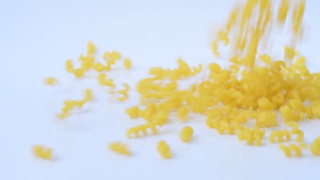 Dry macaroni is strewed on white background in slow motion