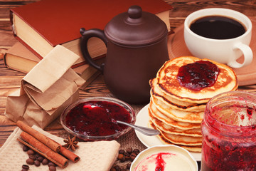Table with stack of pancakes with currant jam and cup of hot coffee