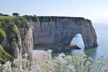 Fototapeta premium ETRETAT, NORMANDY, FRANCE - JUNE 2016: View of Etretat's cliffs and shore from the highland among the flowers across a natural rock opening.