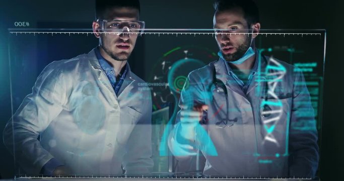 A couple of doctors or scientist analyze the patient's medical situation by checking on a glass monitor with a futuristic holography. Concept of: medicine, doctors, future, holograp