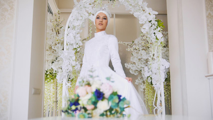Beautiful muslim bride with make up in white wedding dress comes to the flowers