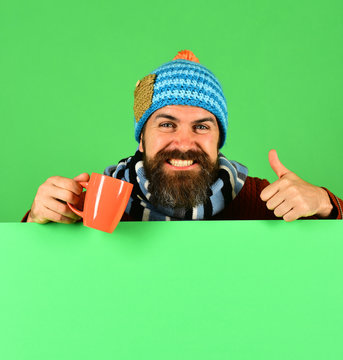 Man in warm hat holds brown cup on green background